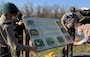 Corps employees unveiling a Native Pollinators information board, part of a Scout Project