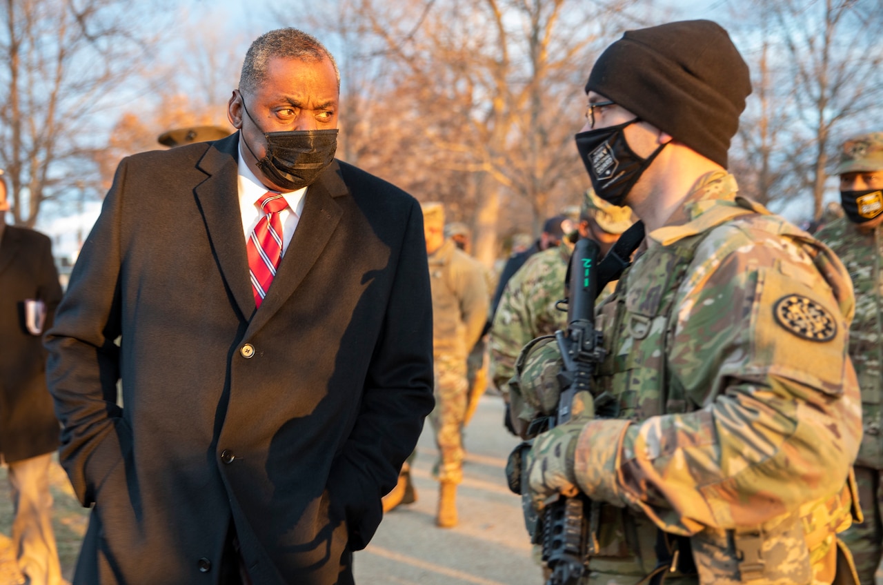 A man in a business suit speaks with a man in a military uniform.