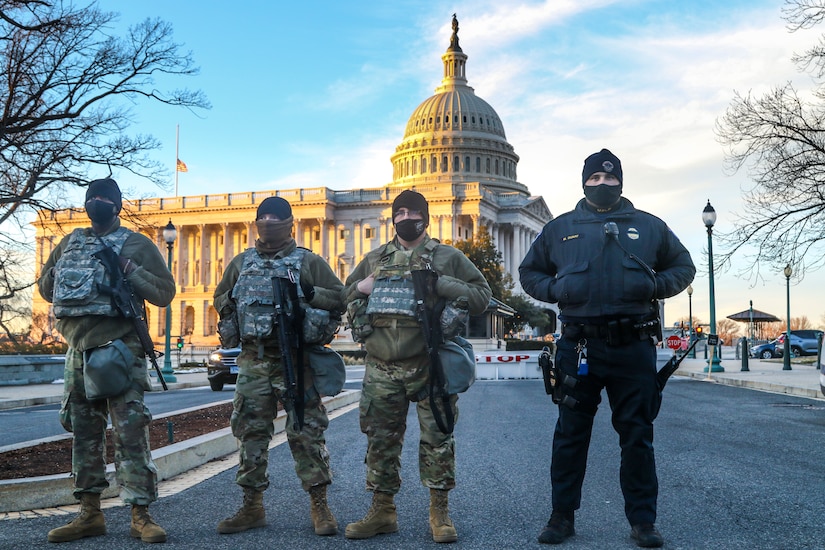 Three men in military uniforms and one man in a police uniform stand near each other in front of the U.S. Capitol.
