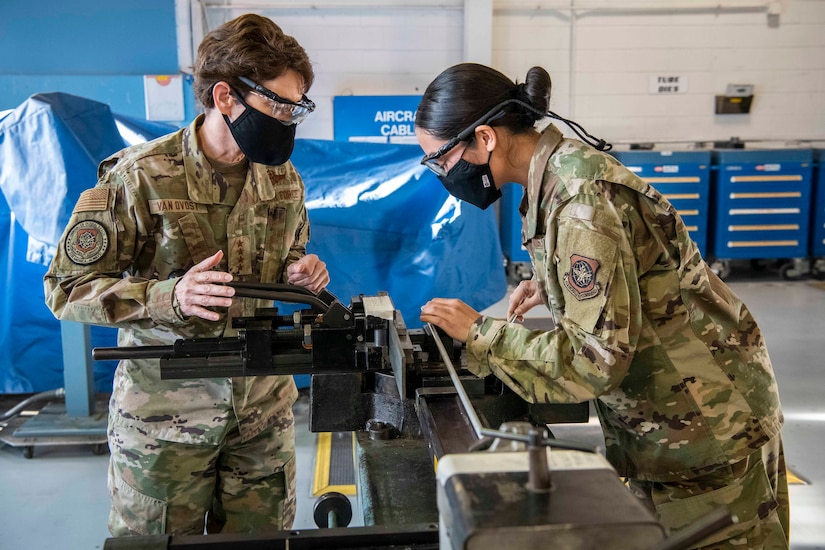 Two airmen manufacture aircraft tubing.