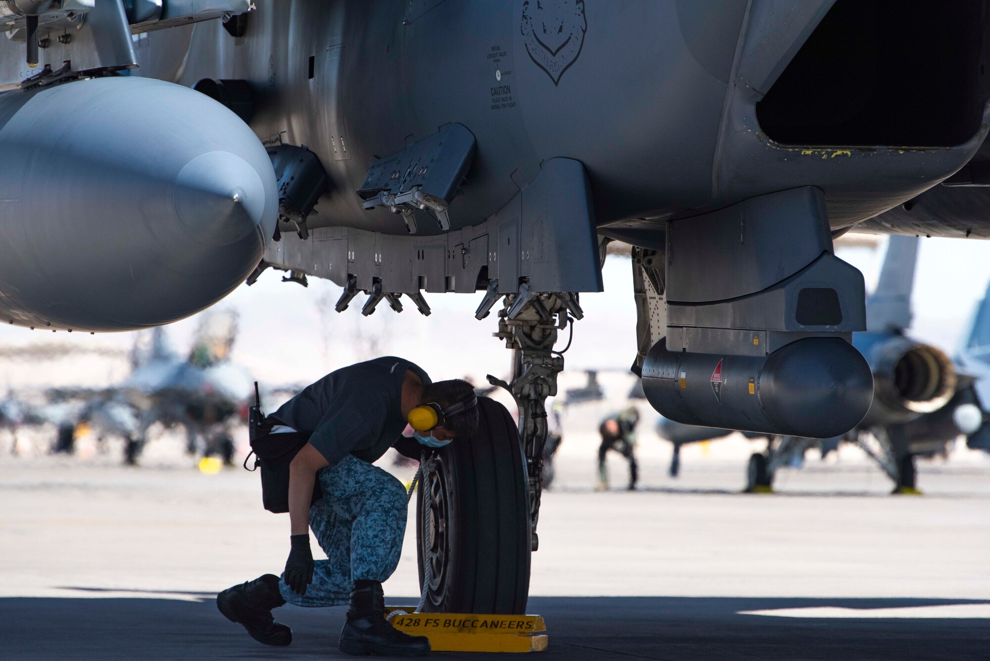 A crew chief from the 428th Fighter Squadron places chocks in front of an F-15SG Strike Eagle’s tire.