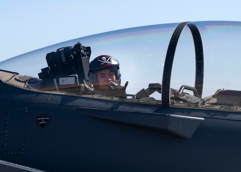 A weapons system operator from the 428th Fighter Squadron holds up a shaka hand symbol from the back seat of an F-15SG Strike Eagle.