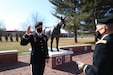 Male soldier in dress uniform raises right hand across from male soldier in dress uniform holding notebook.