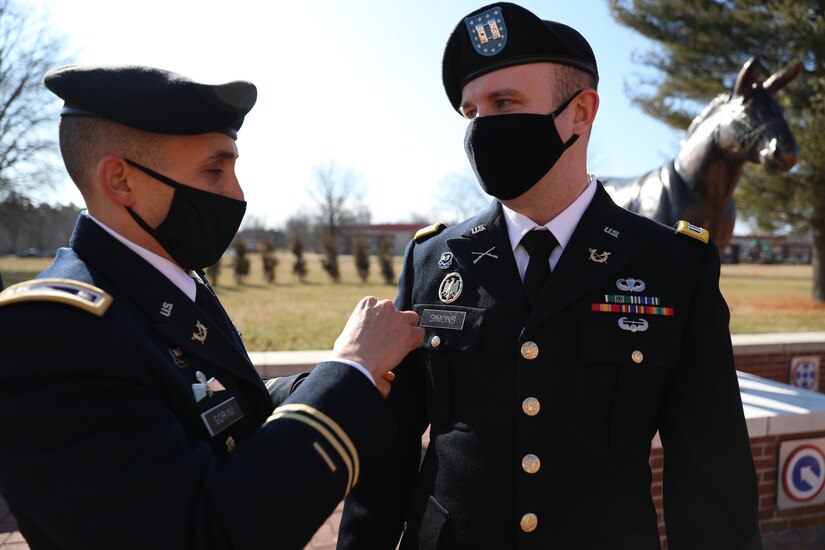 Male soldier in dress uniform pins branch insignia on male soldier in dress uniform.
