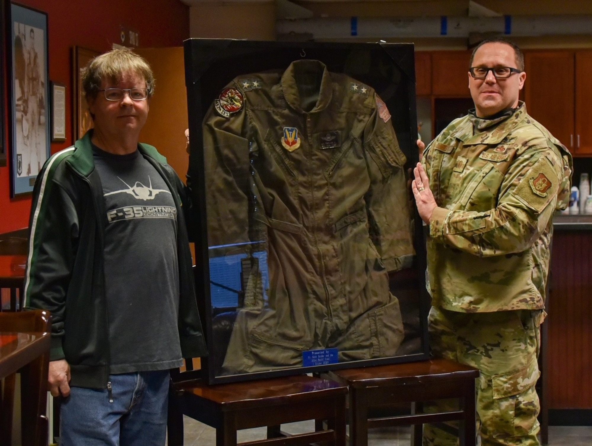(left) Mr. Keith Snyder, local 301st Fighter Wing supporter, and Master Sgt. Troy Quigley, 301st Aircraft Maintenance Squadron weapons load team chief, display the uniform of retired Maj. Gen. John E. Taylor Jr., a former 301st Tactical Fighter Wing commander, on March 7, 2021, at Naval Air Station Joint Reserve Base Fort Worth, Texas.