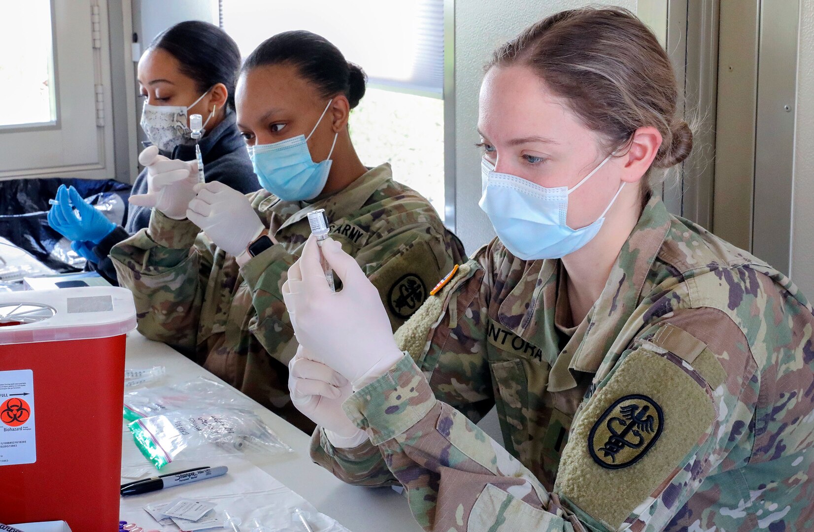 U.S. Army 1st Lt. Abigail Santora (right), a medical surgical nurse at Carl R. Darnall Army Medical Center, Fort Hood, Texas, and 2nd Lt. Sharice Jones (center), a medical surgical nurse at Brooke Army Medical Center, Joint Base San Antonio-Fort Sam Houston, work alongside Federal Emergency Management Agency volunteer medical staff to prepare COVID-19 vaccines at the Fair Park COVID-19 Community Vaccination Centers  in Dallas March 2.