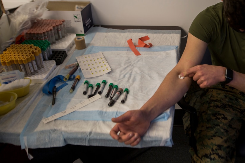 A Marine puts pressure on his arm next to vials of blood samples.