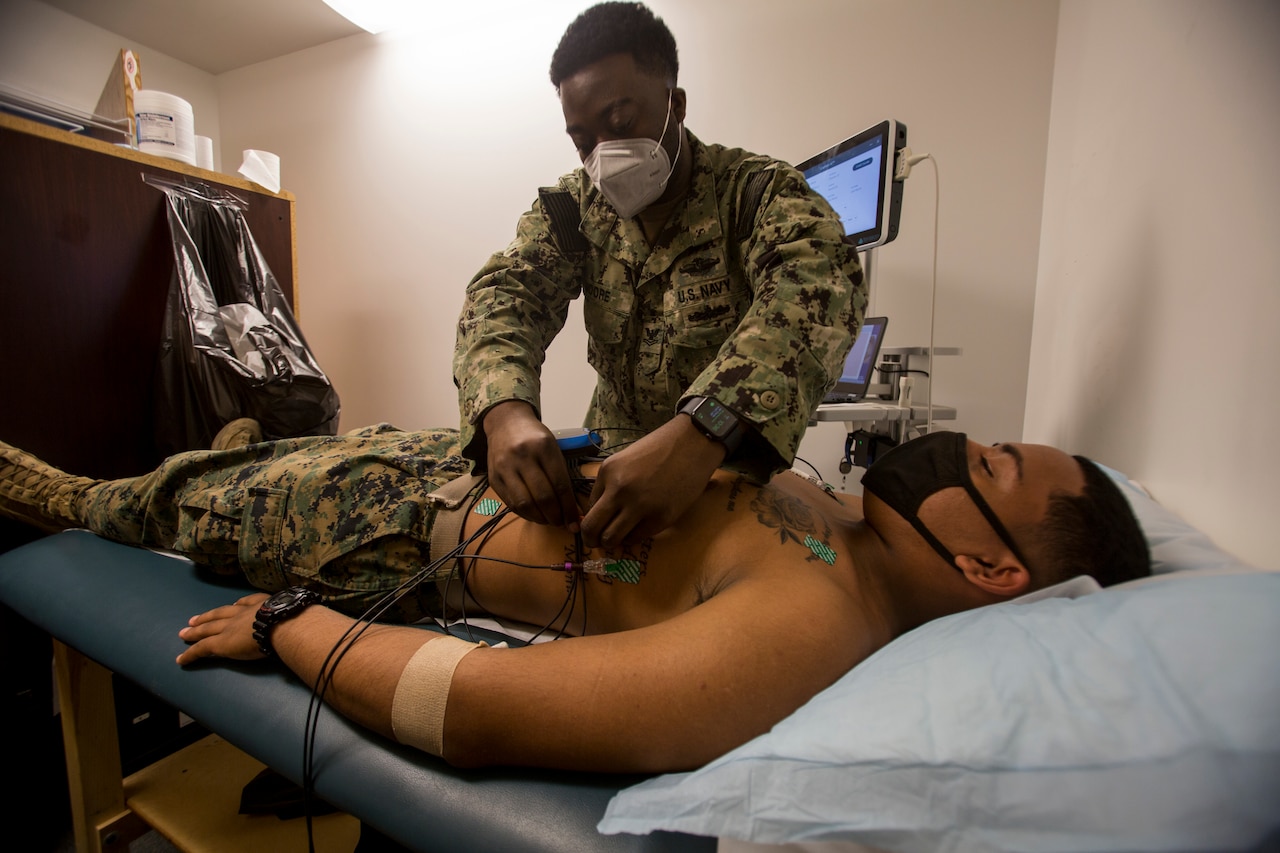 A sailor conducts a health assessment on a Marine attached to medical equipment.