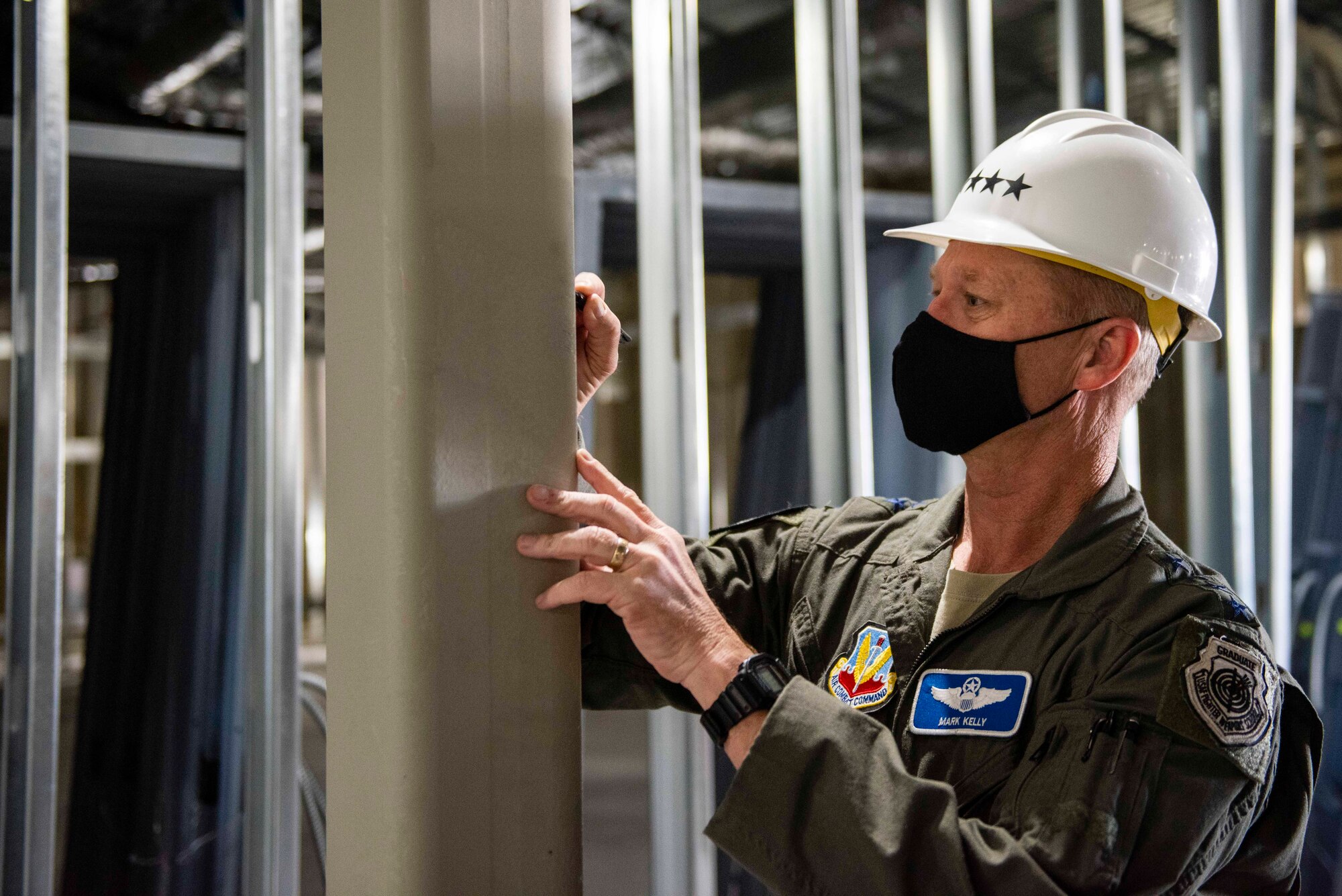 U.S. Air Force Gen. Mark Kelly, commander of Air Combat Command, signs a post in a construction site with steel beams surrounding him.