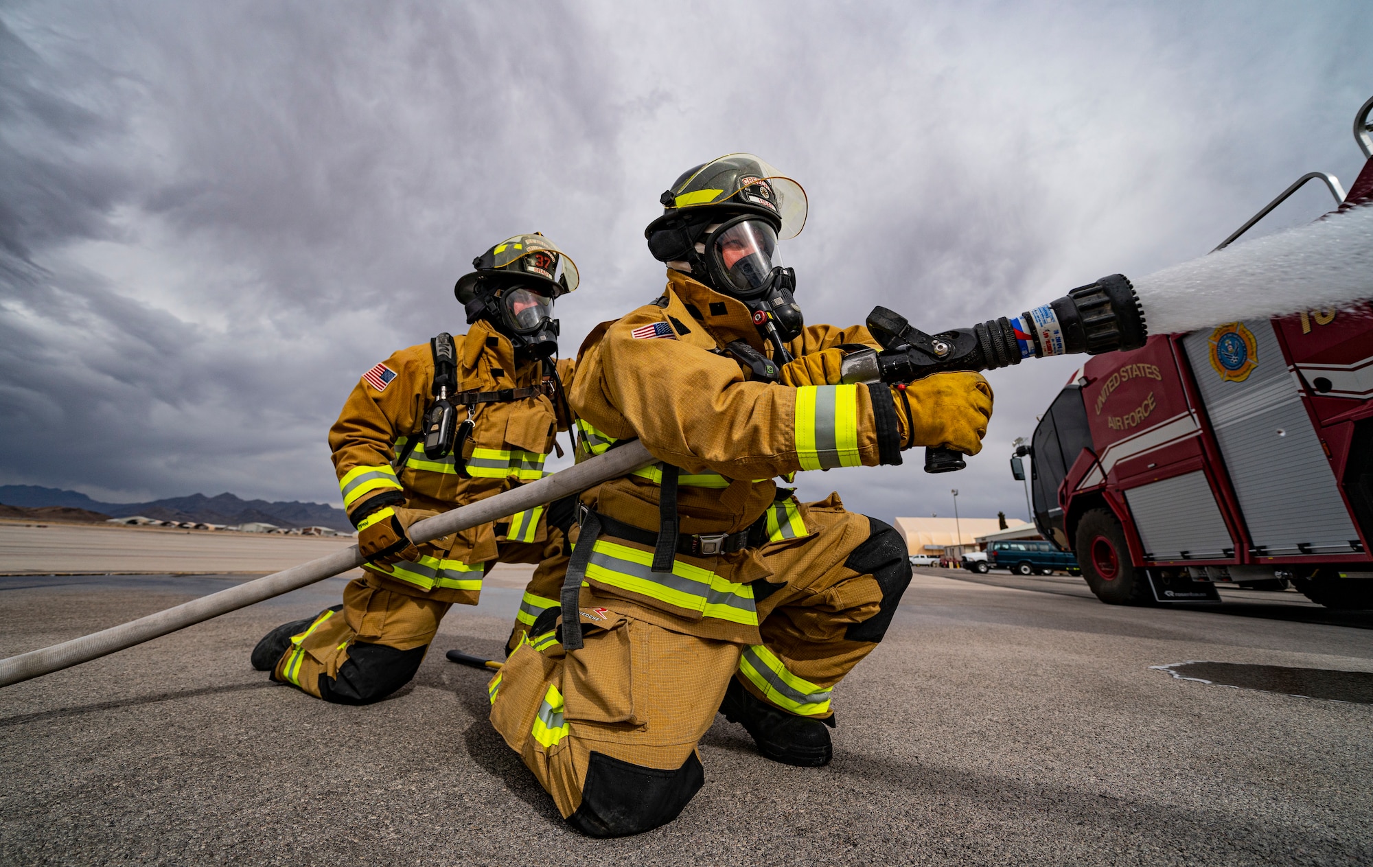 Two members of the Creech Air Force Base fire department employ a firehose.