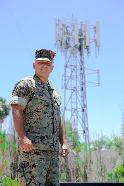 A Marine stands in front of a cell tower.