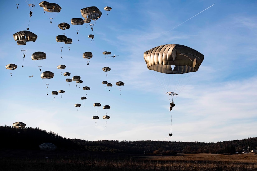 Soldiers wearing parachutes descend in the sky.