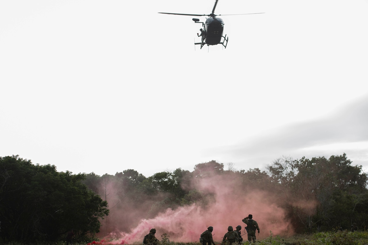 Airmen pop smoke and helicopter raises casualty in a litter in a simulation exercise.