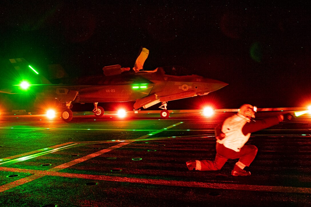 An airman signal an aircraft illuminated by colorful lights.