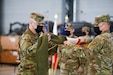 U.S. Army Command Sgt. Maj. Todd Kochte, command sergeant major of the 297th Regional Support Group, left, and Col. Matthew Schell, the commander of the 297th RSG, case the unit colors during a Relief in Place/Transfer of Authority ceremony Feb. 26, 2021, in the hangar of the Powidz Air Base, Powidz, Poland.