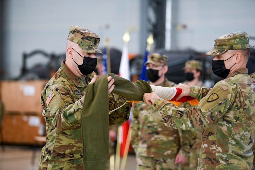 U.S. Army Command Sgt. Maj. Todd Kochte, command sergeant major of the 297th Regional Support Group, left, and Col. Matthew Schell, the commander of the 297th RSG, case the unit colors during a Relief in Place/Transfer of Authority ceremony Feb. 26, 2021, in the hangar of the Powidz Air Base, Powidz, Poland.