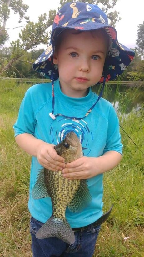 Anthony Gauna III holds a fish he caught by a lake.