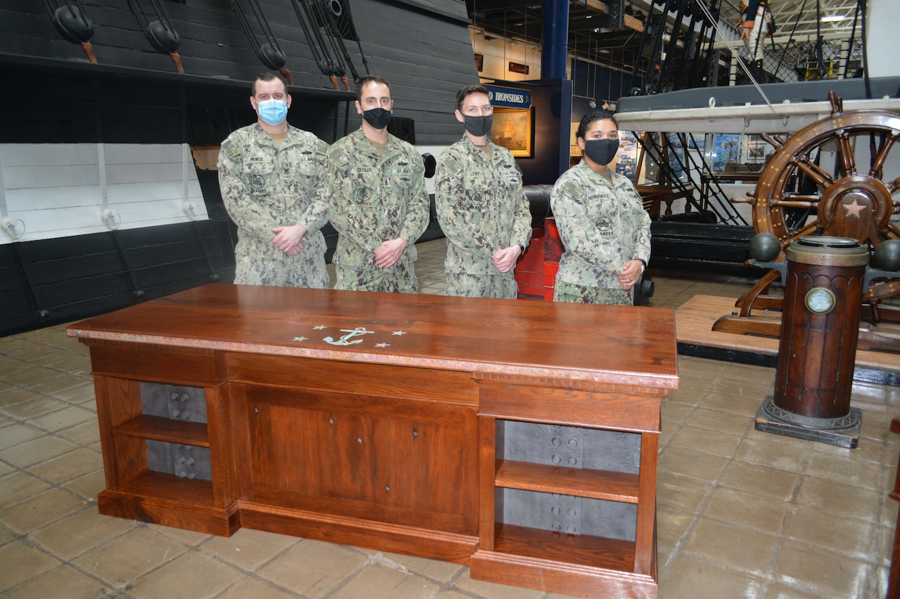 Four sailors stand behind a desk.