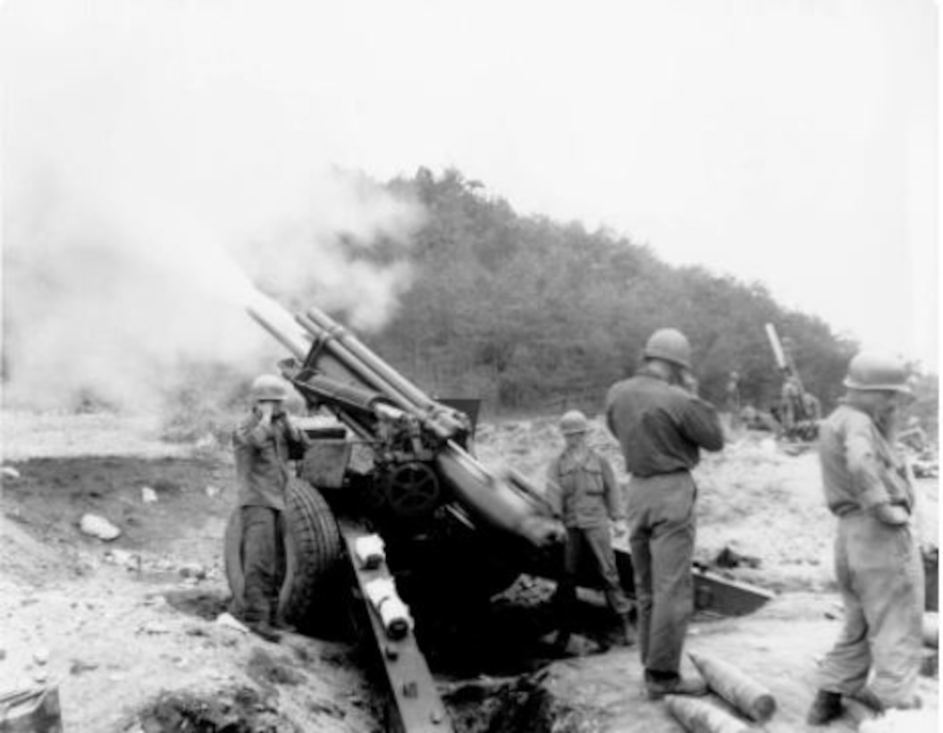 A cloud of rises from a large gun. A few men in military uniforms stand near it.