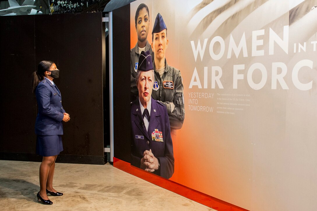 An Air National Guardsman looks at a mural with three female service members on it, including the guardsman.