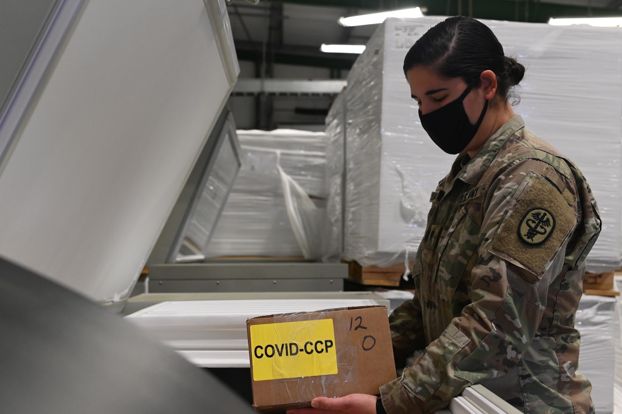 A female Army member sets a box labeled "COVID-CCP" into a refridgerator