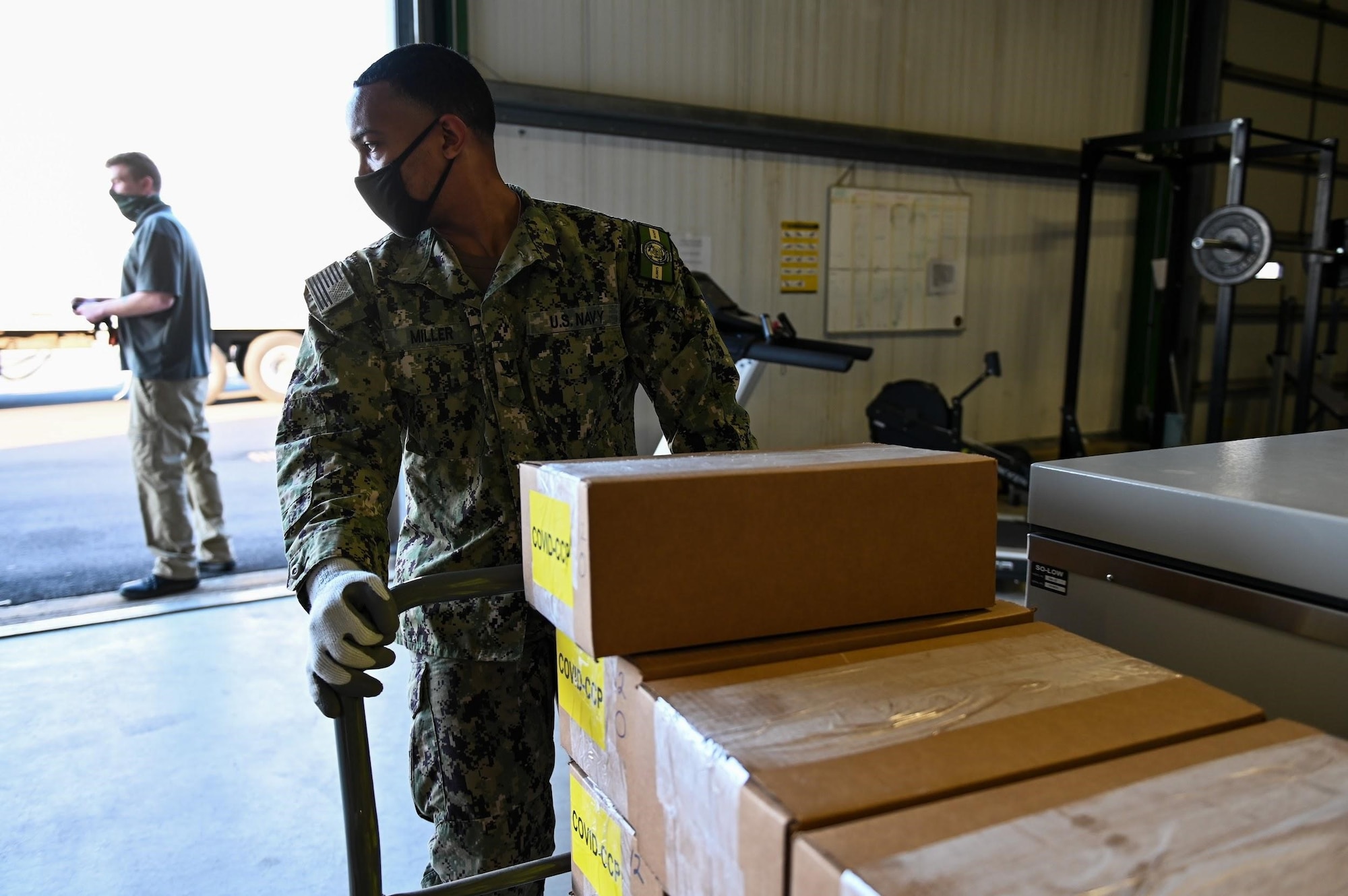 A U.S. Navy Service Member pulls a cart with boxes labeled "COVID-CCP"