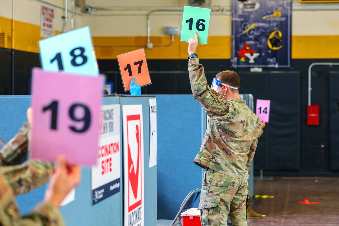 An airman wearing a face mask holds up a card with a number on it.