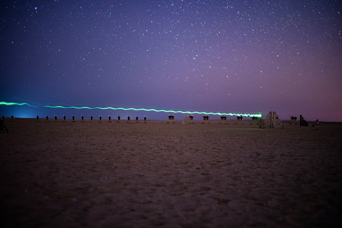 Marines run on sand under a starry sky illuminated by a blue streak.
