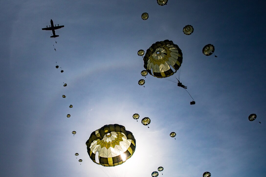 Paratroopers descend from an aircraft using parachutes.