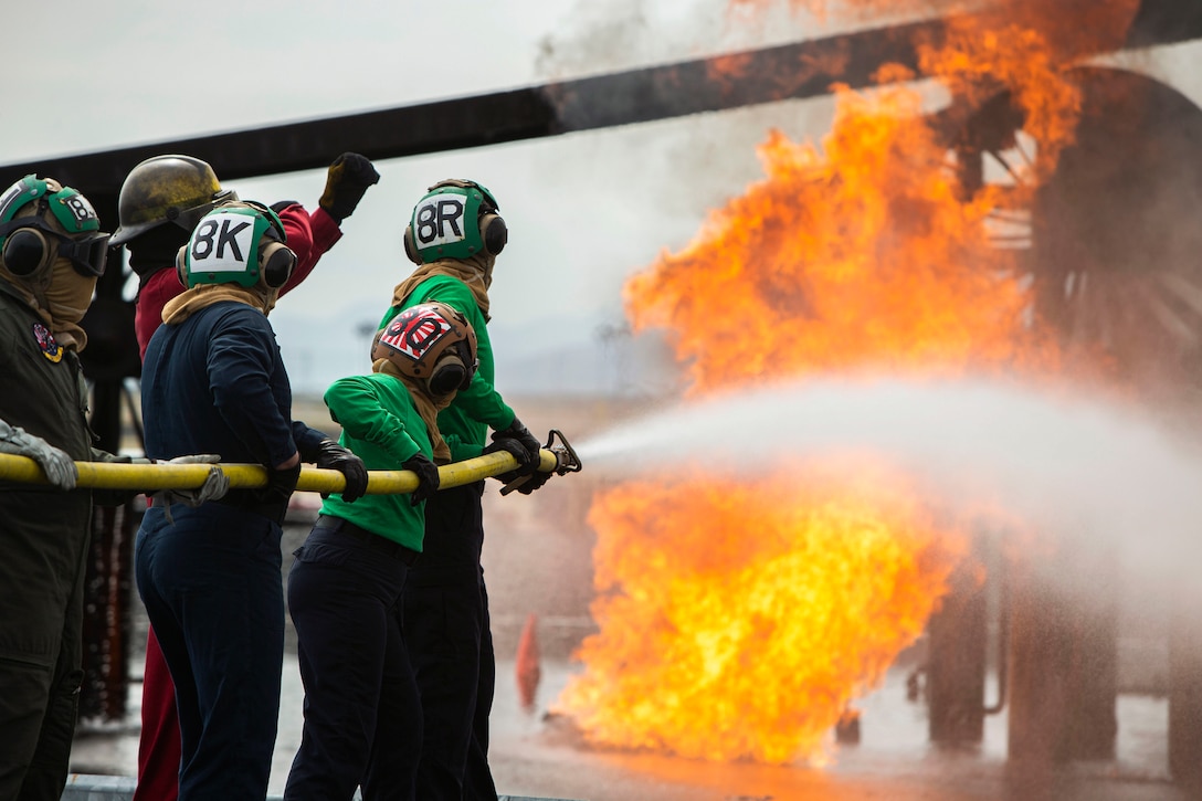 Sailors use a water hose to put out a fire.