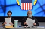 Two masked DLA employees open sealed bid envelopes.