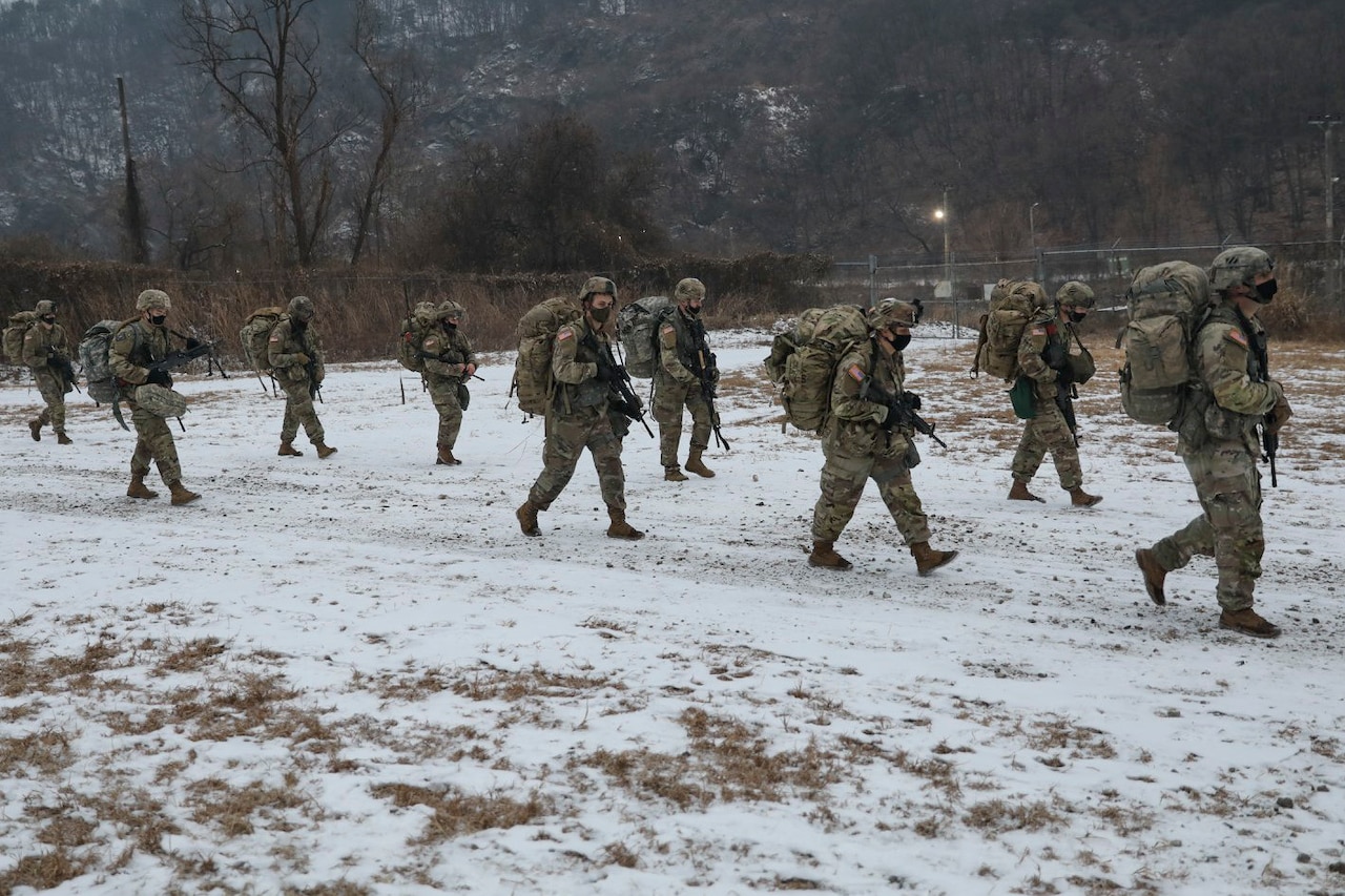 A group of soldiers march along a snow-covered trail.
