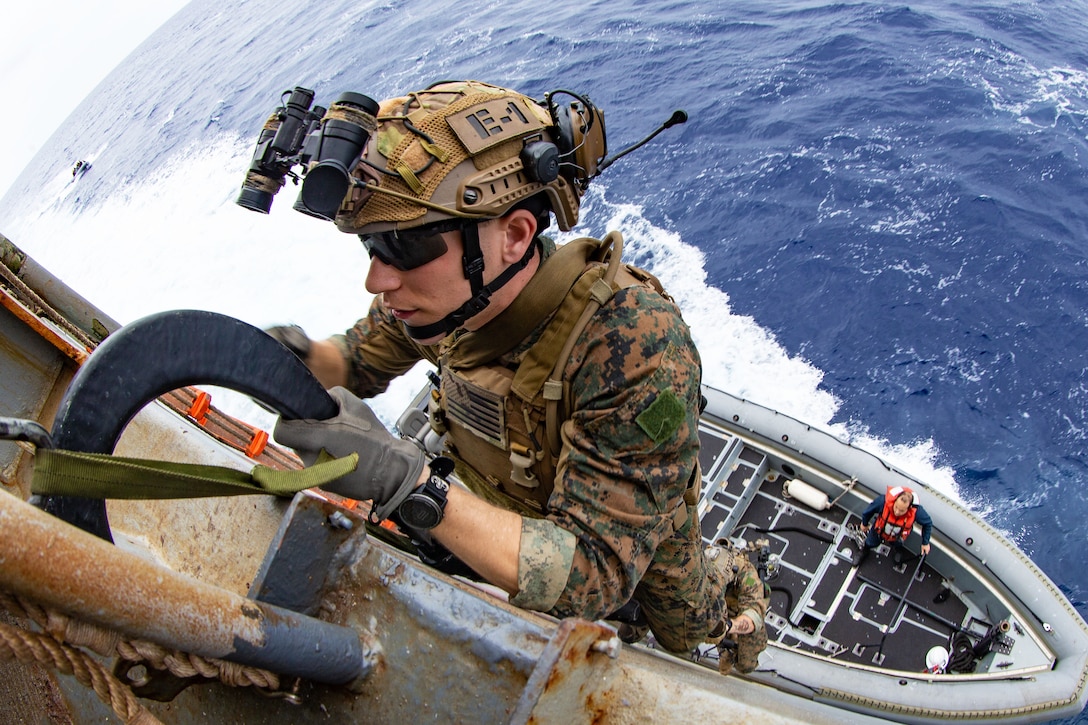 A Marine climbs from a water craft onto the side of a ship.