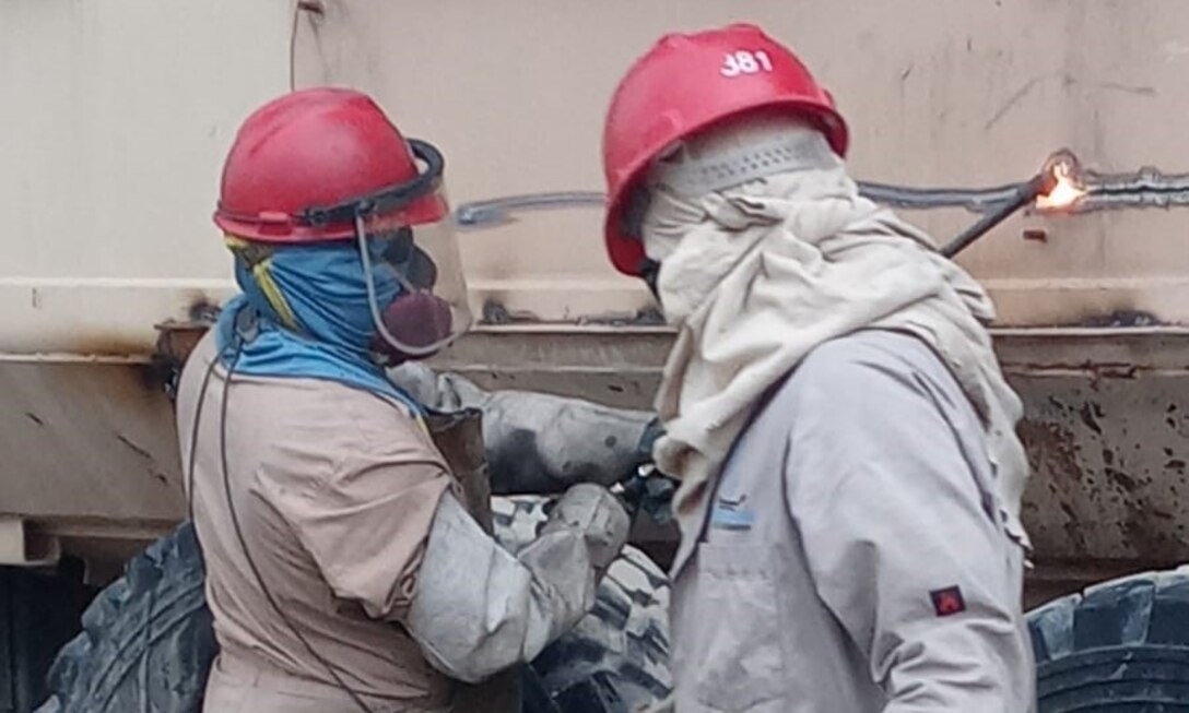 Contractor employees at DLA Disposition Services' Camp Arifjan, Kuwait, site work together as one manages the hoses supplying the cutting torch used by his colleague as they demilitarize a large mine-resistant, ambush protected vehicle.