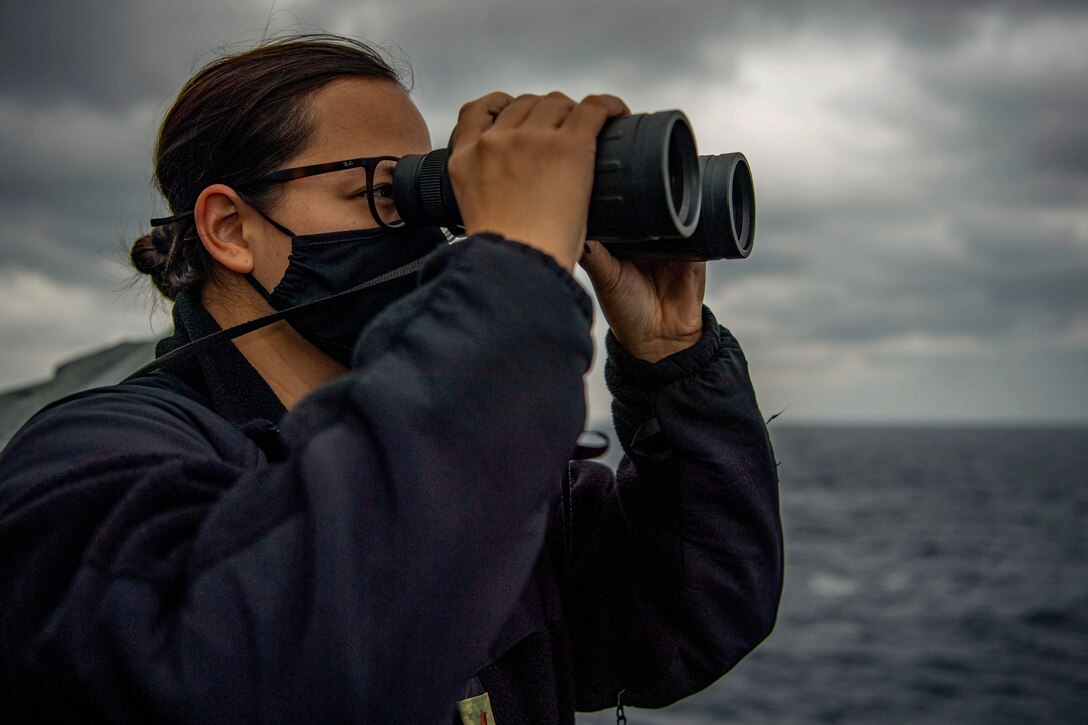 A sailor uses binoculars while on a ship at sea.