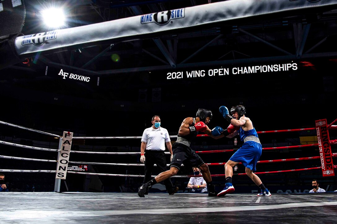 Two boxers face each other in a boxing ring as a referee stands to the side.