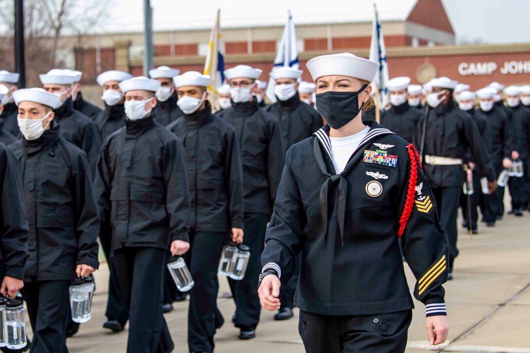 A sailor marches in formation next to a group of other sailors.