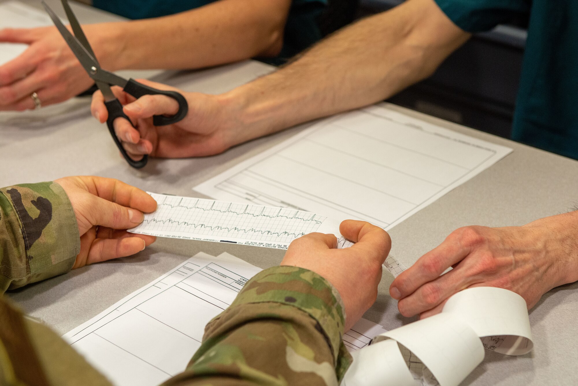 U.S. Air Force Master Sgt. Daniel Bierl, holding paper strip, 673d Inpatient Operations Squadron flight chief, and U.S. Air Force Chief Master Sgt. Lee Mills, holding scissors, JBER and 673d ABW command chief, practice cardiac tracing during a 673d IPTS immersion at Joint Base Elmendorf-Richardson, Alaska, Feb. 26, 2021. The tour familiarized base leadership with the 673d IPTS and its role in supporting readiness. The 673d IPTS provides a full range of medical care to include perinatal care, intensive care, and behavioral health services to JBER and the greater Anchorage area.