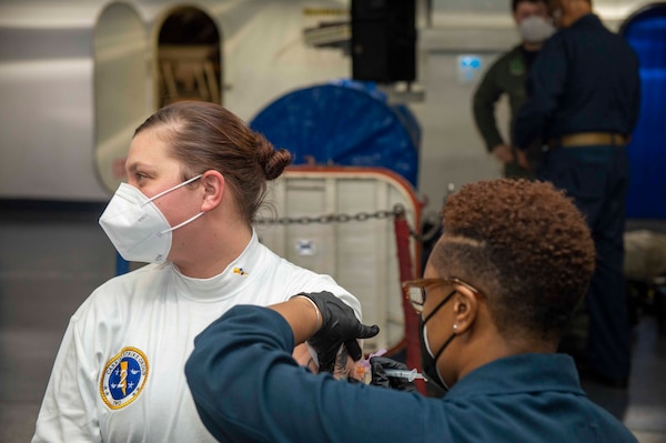 Fire Controlman 1st Class Jessica Kelahan, from Woodstock, Illinois, receives a second dose of the COVID-19 vaccination from Hospital Corpsman 1st Class Autumn Nichols.
