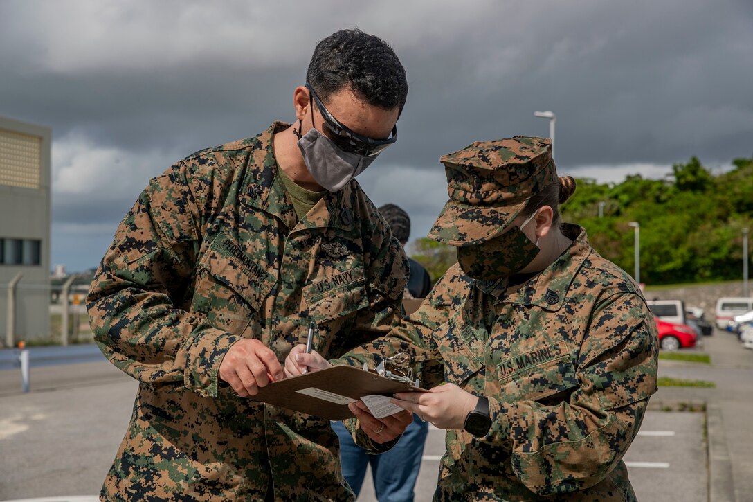 U.S. Navy Petty Officer 1st Class Jay Perezmontanez, a health service support operational chief with Marine Rotational Force Darwin, helps U.S. Marine Corps Staff Sgt. Felicia White, a supply chief with Camp Kinser Post Office, check in to receive her second dose of the COVID-19 vaccine at the U.S. Naval Hospital Okinawa, on Camp Foster, Mar. 2, 2021. On Jan. 11, 2021, active duty personnel were permitted to receive the vaccine. As service members receive the second dose of the vaccine, they are given a sticker stating ‘I got my COVID-19 vaccine because…’ This personal memento signifies their own unique reason to receive the vaccine. White is a native to El Paso, Texas and Perezmontanez is a native to Orange Park, Florida. (U.S. Marine Corps photo by Lance Cpl. Zachary Larsen)