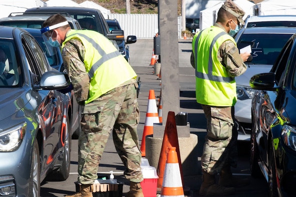 Two soldiers speak with Californians getting a vaccine in a drive-up facility.
