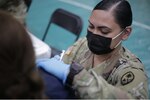 Spc. Heather Nera of Task Force Medical, Joint Task Force 671, Guam National Guard, administers a dose of COVID-19 vaccine to a patient at the University of Guam Calvo Field House on her birthday, Feb. 6, 2020. On March 11, 2021, Guam ranked No. 4 among all states and territories in doses administered per 100,000 people, according to the Centers for Disease Control and Prevention COVID Data Tracker website.