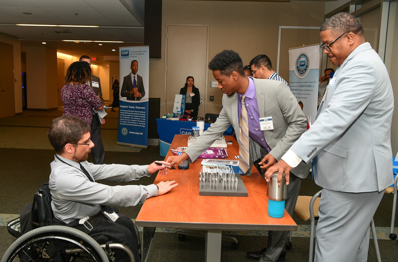 A man behind a display desk hands a man in a wheelchair a pen-like device.