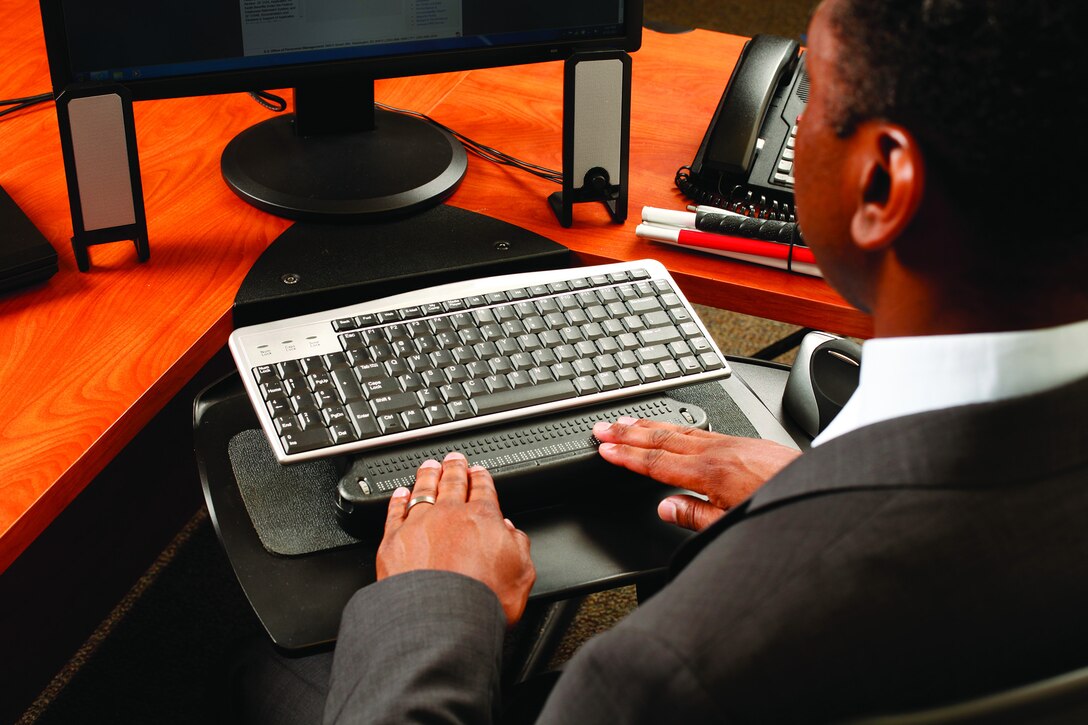 A man holds his hands over a keyboard attachment that allows him to read Braille.
