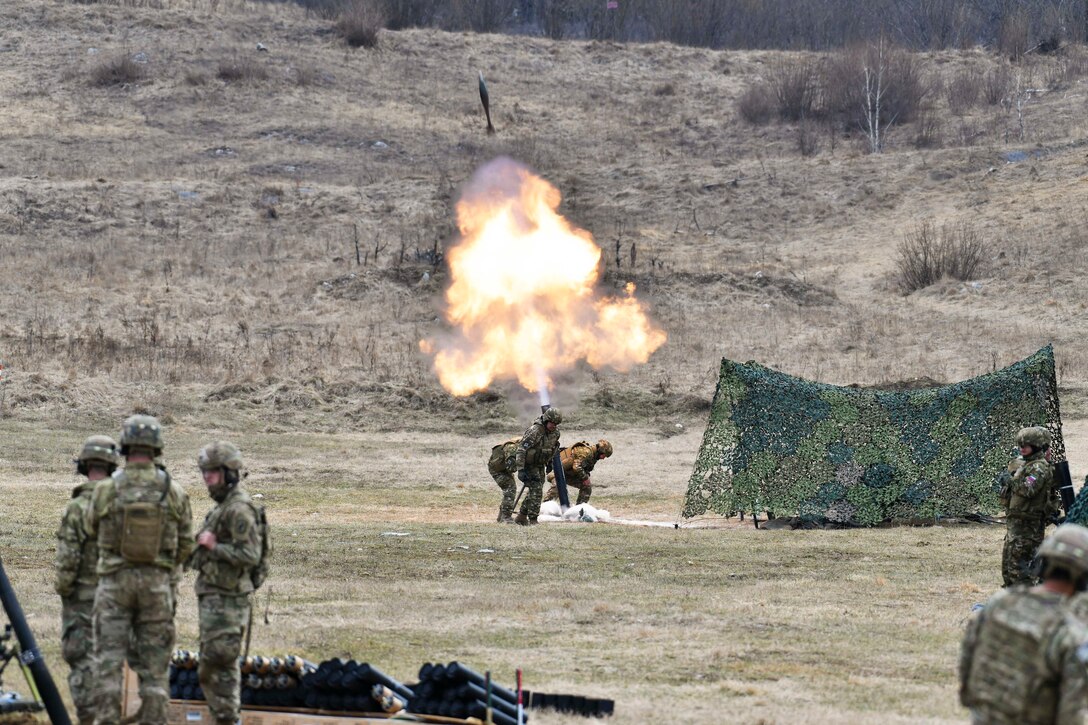 Troops fire a weapon in a field.