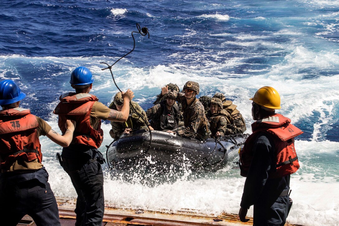 Marines throw a rope from a ship to fellow Marines riding in a boat.
