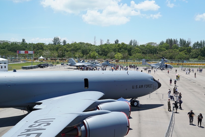 People walk on a tarmac looking at large planes.