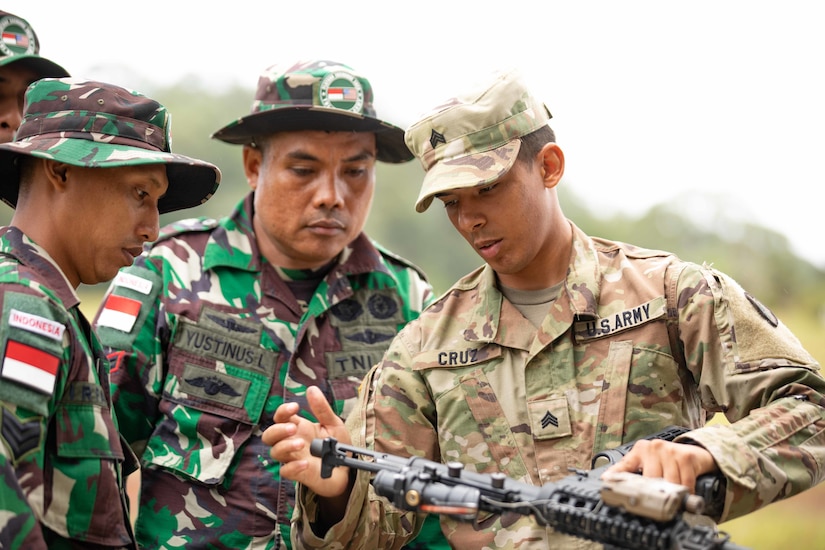 A soldier holding  a gun speaks to other soldiers.