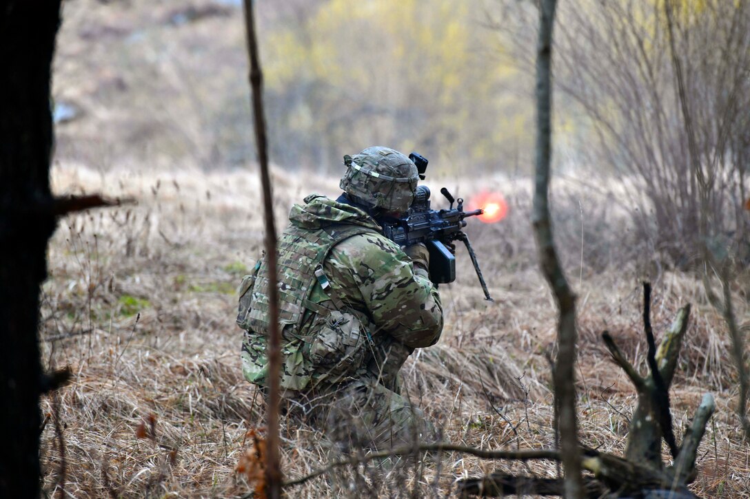 A soldier fires a weapon in the woods.