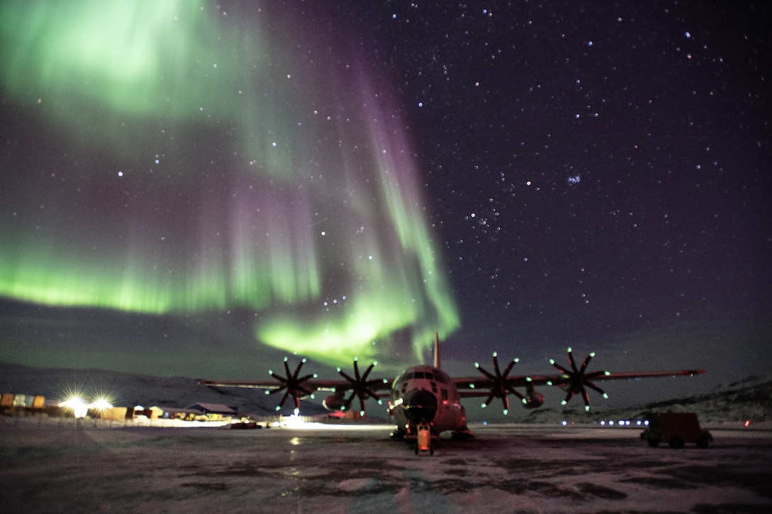 Green light covers most of the sky above a military aircraft on the tarmac at night.